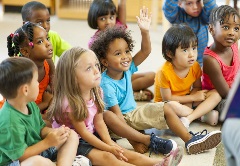 Young children sitting on the floor listening intently to an adult reading a story
