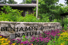 Picture of a rock wall that says Benjamin Olewine Nature Center with building in the background and wildflowers in the foreground