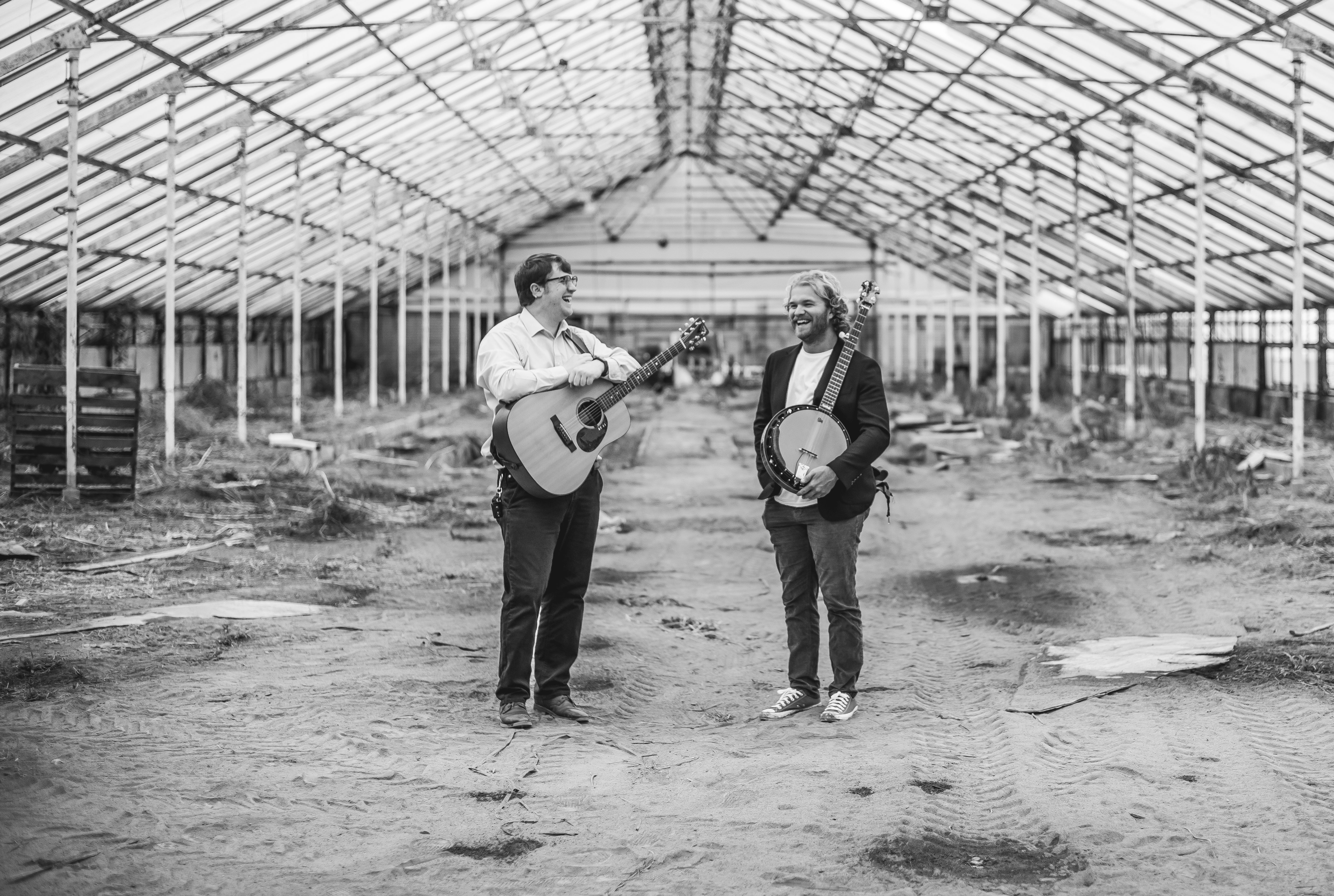 Two male musicians one with a guitar and one with a banjo in a greenhouse
