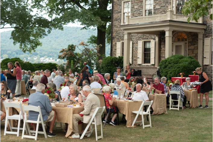 People enjoying an elegant dinner on the lawn of a historic mansion.