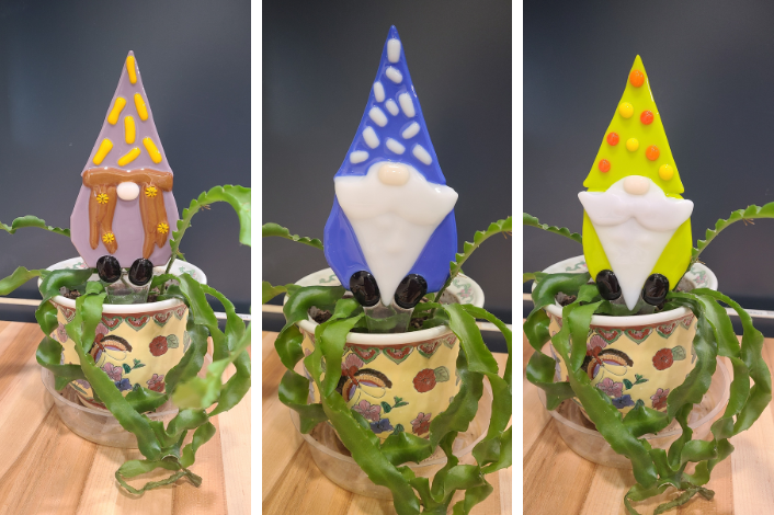 Fused glass gnomes of various colors sitting in potted plants