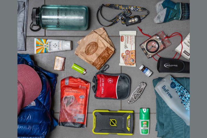 Photo of essential packing items for camping - sleeping bag, sunscreen, water bottle, first aid kit, insect repellant, socks, etc.
